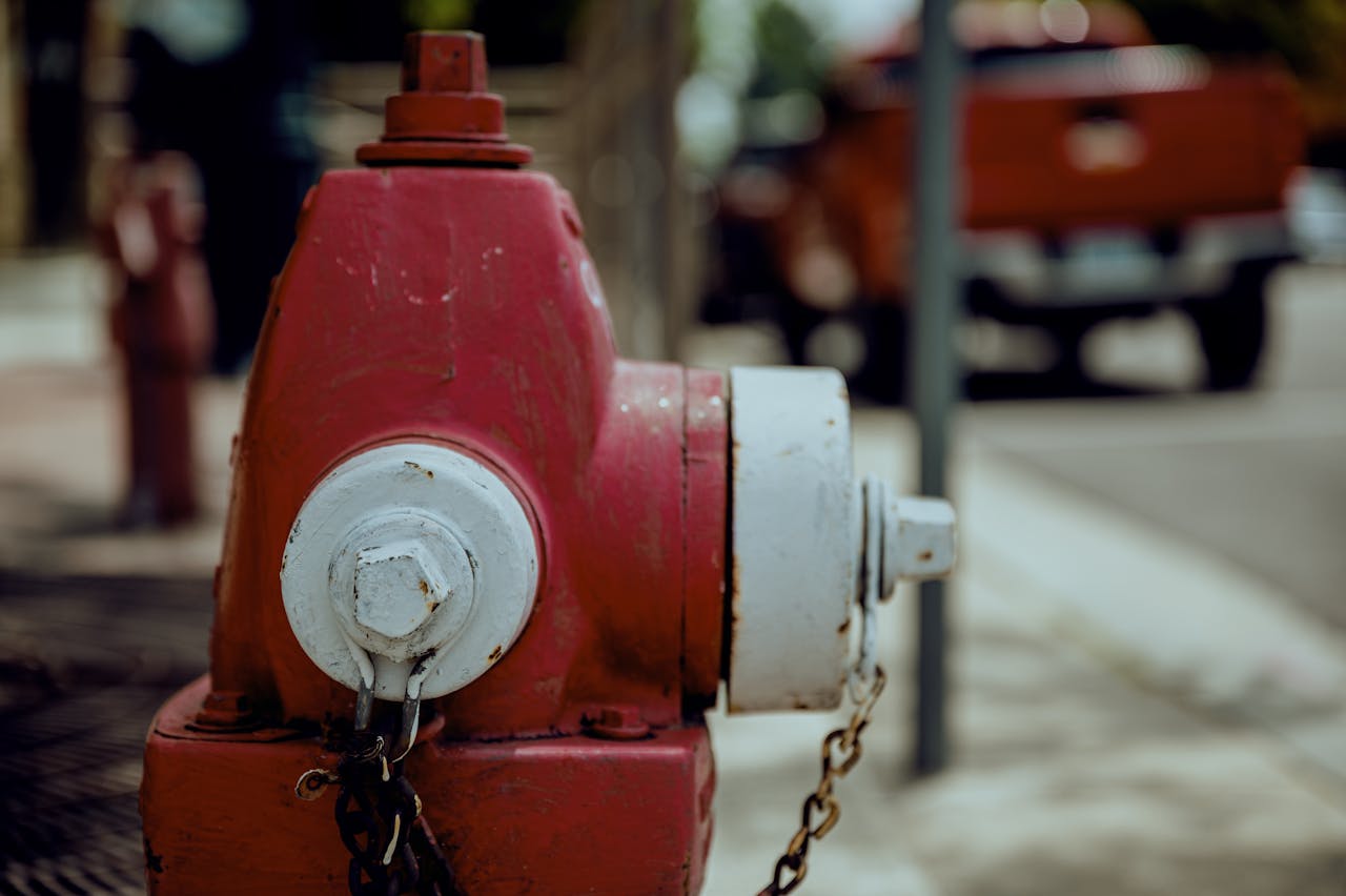 Shabby red and white metal fire hydrant with rusty chain located on city street in daytime